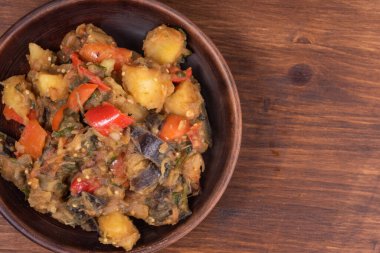 Traditional Italian vegetable stew with potatoes, eggplant, tomatoes and peppers in a rustic earthenware plate on a woody background, copy space - Neapolitan style cianfotta.