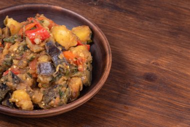 Traditional Italian vegetable stew with potatoes, eggplant, tomatoes and peppers in a rustic earthenware plate on a woody background, copy space - Neapolitan style cianfotta.