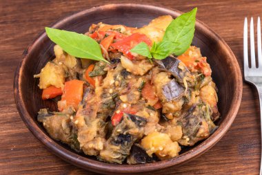 Italian vegetable stew with potatoes, eggplants, tomatoes, pepper in a rustic clay plate, decorated with fresh basil leaves on a woody background - Ciambotta, cianfotta in Neapolitan style.
