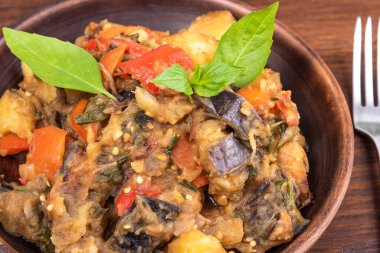Italian vegetable stew with potatoes, eggplants, tomatoes, pepper in a rustic clay plate, decorated with fresh basil leaves on a woody background - Ciambotta, cianfotta in Neapolitan style.