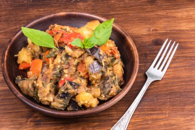 Italian vegetable stew with potatoes, eggplants, tomatoes, pepper in a rustic clay plate, decorated with fresh basil leaves on a woody background - Ciambotta, cianfotta in Neapolitan style.