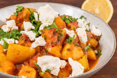 Yunan sebze ve patates yahnisi domates sosunda, ahşap bir masada, üst tarafta, yakın planda, tabakta yumuşak feta peyniri parçaları ile.