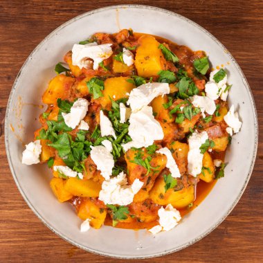 Yunan sebze ve patates yahnisi domates sosunda, ahşap bir masada, üst tarafta, yakın planda, tabakta yumuşak feta peyniri parçaları ile.