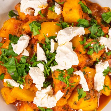 Yunanca patates ve sebze güveci domates sosu içinde yumuşak feta peyniri ile ahşap bir masada, üst manzara, macro