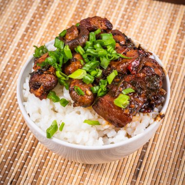 Baharatlı domuz etli küçük kâse baharatlı mantar, acı biber ve haşlanmış pirinç bambu peçetesi ve çubuk üzerine doğranmış yeşil soğan serpiştirilmiş.