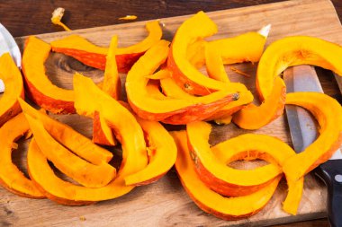 Balkabağı, ahşap mutfak kesme tahtası ve büyük bir bıçakla pişirmek için küçük parçalara bölünmüş.