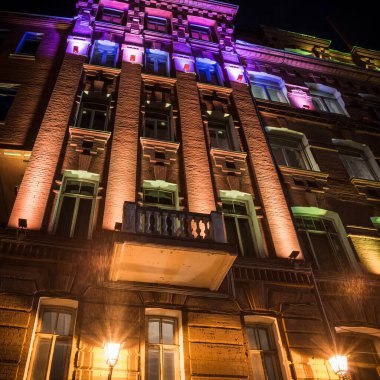 Eski büyük tuğladan bir binanın ön cephesi. Geceleri çok güzel aydınlatması olan bir balkon.