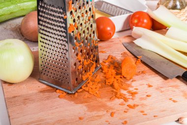 Vejetaryen yemeği hazırlamak için mutfak tahtasına sebze rendesi ve rendelenmiş havuç.