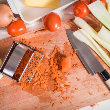 Vejetaryen yemeği hazırlamak için mutfak tahtasına sebze rendesi ve rendelenmiş havuç.