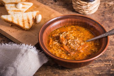 Kil bir kase ve kaşıkta sebzeli pirinç çorbası, kızarmış ekmekle birlikte ahşap bir masa - sağlıklı bir İtalyan yemeği.