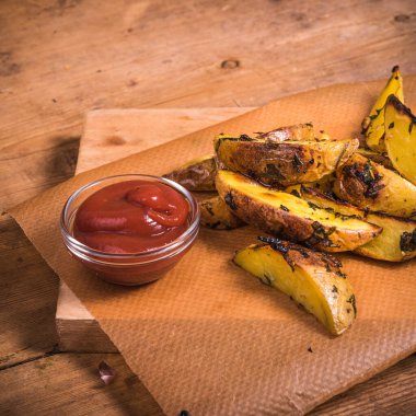 Ahşap bir tahta üzerinde, ahşap bir masanın üzerinde, yakın planda pişirilmiş patates dilimleri ve sos.