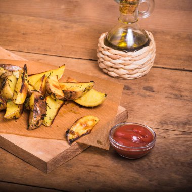 Ahşap bir tahta üzerinde, ahşap bir masanın üzerinde, yakın planda pişirilmiş patates dilimleri ve sos.