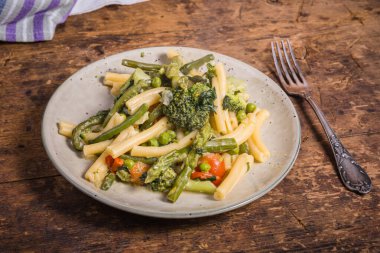 Vejetaryen amerikan ve İtalyan primavera makarna tabağı brokoli, fasulye, kuşkonmaz, bezelye ve domatesler ahşap bir masada, üst manzara