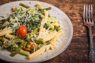 Vejetaryen Amerikan ve İtalyan primavera makarna tabağı brokoli, fasulye, kuşkonmaz, bezelye ve domatesler ahşap bir masada, üst manzara, yakın çekim.