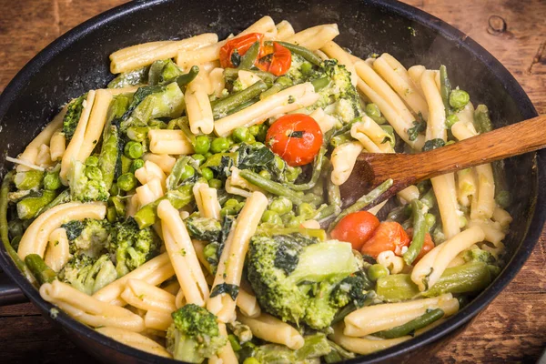 素食美式和意大利式的原味意式意式面食 配上西兰花 豌豆和西红柿 放在木制桌子上的煎锅里 尽收眼底 — 图库照片