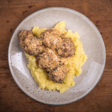 Swedish chicken meatballs with cheese in a creamy sauce with mashed potatoes in a plate on a wooden table, close-up, top view