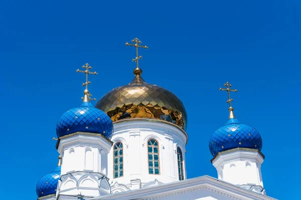 Golden and blue domes with crosses of an Orthodox church against a blue sky