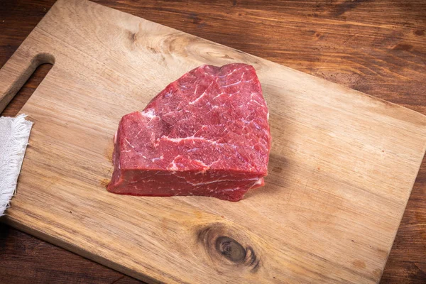 Ahşap mutfak kesme tahtasının üzerinde taze çiğ et parçası.