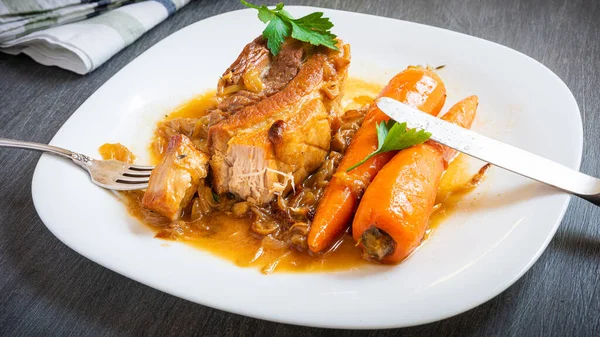 Traditional American restaurant dish - fried pork belly with carrots, large serving on a white plate