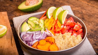 Vejetaryen sağlıklı yemek kasesi - dilimlenmiş domates, avokado, biber, soğan ve havuç ve ahşap masa üzerinde kaynatılmış kinoa, harika bir plan.