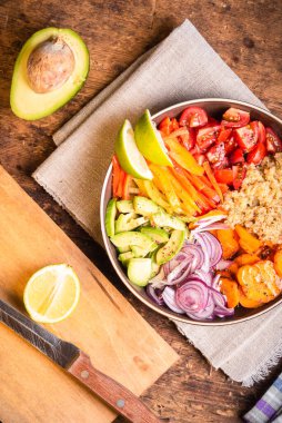 Vejetaryen sağlıklı yemek kasesi - dilimlenmiş domates, avokado, biber, soğan ve havuç ve ahşap bir masada limon dilimleri ile kaynatılmış kinoa, yakın çekim, üst görüş
