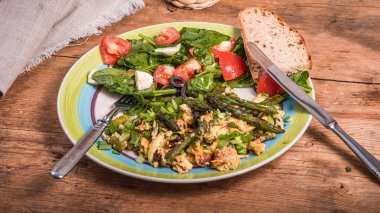 Amerikan sahanda yumurta, kuşkonmaz, ıspanak ve domates kırsal ahşap bir masada büyük bir tabakta - basit bir köy kahvaltısı.