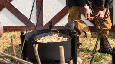 Ortaçağ kıyafetleri içinde şef, caddede tavada etli arpa lapası pişirir.