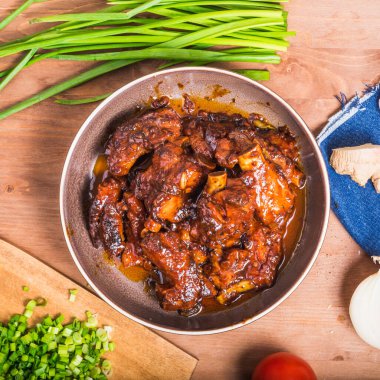 Baharatlı bir sosta, ahşap bir masada pişirilmiş domuz pirzolası ve soğan, zencefil, domates gibi malzemeler. Domuz pirzolası - Karayip mutfağı