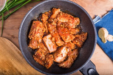 Baharatlı sosta marine edilmiş domuz eti parçaları en iyi tavada pişirilir. Baharatlı çiğ domuz eti ve ahşap masa