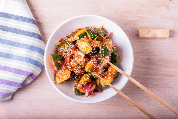 Kimchi soslu baharatlı Kore salatası. Masada yemek çubukları olan bir kasede susam tohumları var.