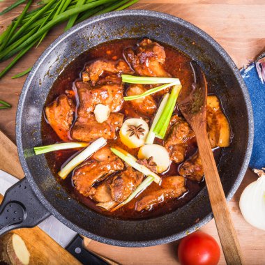 Baharatlı domuz güveci pişiriyorum. Baharatlı soslu domuz parçaları, malzemeler, soğan, zencefil ve yıldız anasonu bir tavada, üst manzara, yakın çekim