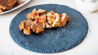 Teriyaki tavuğu dilimlenmiş ve susam tohumları serpiştirilmiş ve kırmızı biberler tahtaya serpiştirilmiş.