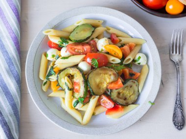 Sıcak yaz İtalyan salatası makarna, kızarmış kabak, domates ve mozzarella peyniri tabakta.