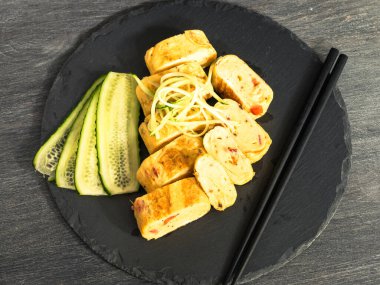 Japon tamago omleti. Salatalıklı. Yemek çubuklarıyla servis tahtasında.