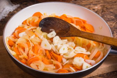 Sebze sosu pişirmek - soğan, havuç ve sarımsak bir tavada pişiriliyor, ahşap kaşıkla yakın plan çekimde.