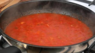 Tavada ev yapımı domates sosu pişirmek, yakın plan. Domates, sarımsak ve fesleğenli İtalyan marinara sosu tavada kaynıyor..