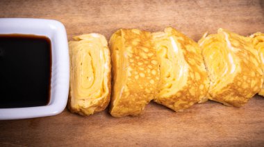 Japon omleti tamago yaki ahşap bir tahtanın üzerinde soya sosu ile rulo şeklinde.