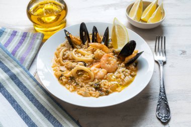 Sehpadaki tabakta deniz ürünleri, karides, kalamar halkaları ve midye ile bir sürahi zeytinyağı ve limon dilimleri ile risotto.