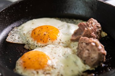 Yumurtalar dökme demir bir tavada et parçalarıyla kızartılır..