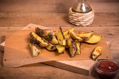 Ahşap bir tahtanın üzerinde bir fincan domates sosuyla fırında patates kamışı.