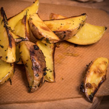 Ahşap bir tahta üzerinde otlu fırında patates dilimleri.