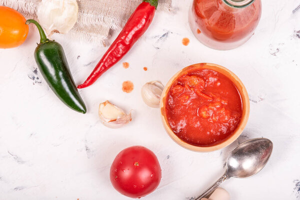 Ingredients for making mexican hot sauce - tomatoes, chili and jalapenos, garlic, chopped tomatoes in a cup and ready-made sauce in a bottle on a light background, top view, flat lay