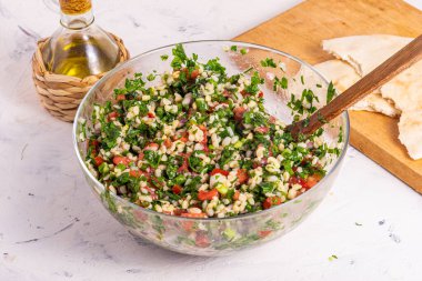 Tabbouleh salatası pişirmek - malzemeleri cam bir kâse içinde karıştırmak bir lamba masasında tahta bir kaşıkla