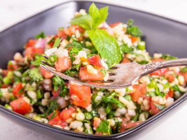 Geleneksel Lübnan Tabouleh salatası siyah bir fincanda nane yaprakları ve ön planda salatayla süslenmiş bir çatal..