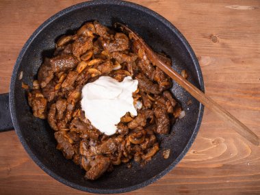 Tencerede şampiyonlarla sığır stroganoff pişirmek neredeyse bitmiş bir tabağa ekşi krema eklemek, üst manzara..