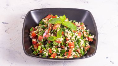 Geleneksel Arap tabbouleh salatası, açık arkaplanda siyah bir kasede bulgur var.