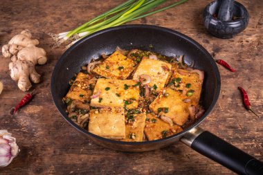 Baharatlı sosla pişirilmiş soya peyniri, soğanlı, kırsal ahşap bir masada kızartma tavası, yakın plan.