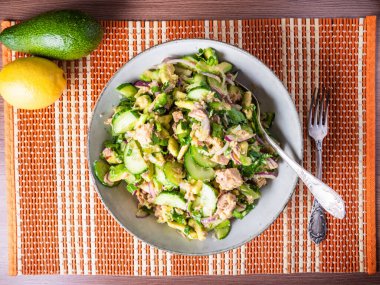 Bir tabak bambu peçetesinde konserve ton balığı, avokado, salatalık ve soğanlı salata.