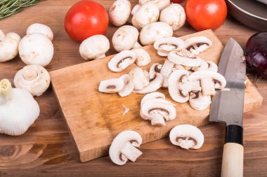 Mantar yahnisi hazırlıkları. Doğranmış çiğ şampiyonlar. Kesme tahtası, domates, soğan ve sarımsak.