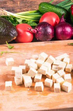 Mutfak tahtasında doğranmış tofu peyniri ve salata için sebze, yakın plan.
